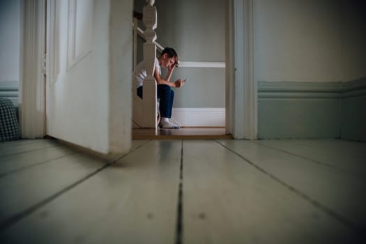 Boy sitting at the bottom of the stairs using a smartphone.