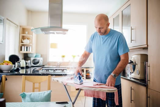 Mature man ironing laundry in the kitchen.