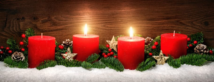Low-key studio shot of elegant advent decoration with fir branches on snow and tow burning red candles,dark wood background