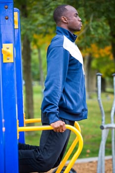 Active black man in training suit exercising at outdoor gym
