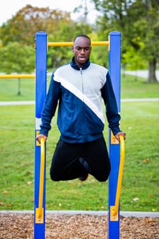 Active black man in training suit exercising at outdoor gym