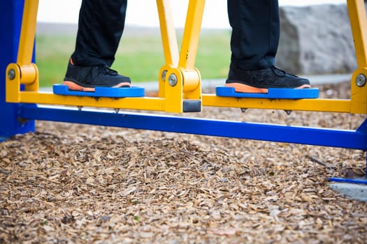 Active man in training suit exercising on elliptical trainer machine at outdoor gym
