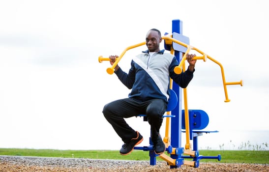 Active black man in training suit exercising at outdoor gym