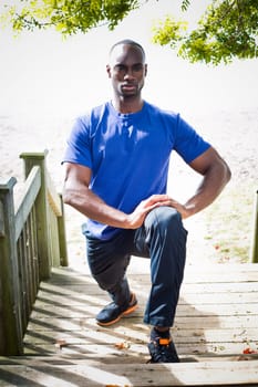 young black man wearing athletic wear sitting on the beach exercising yoga