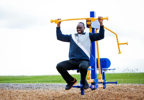 Active black man in training suit exercising at outdoor gym