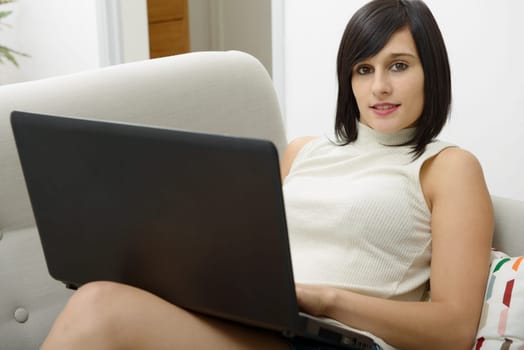 young brunette girl student sitting on the couch with a laptop