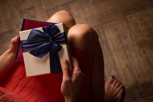 Top view woman opening a present with blue ribbon with three gift boxes inside on her knees