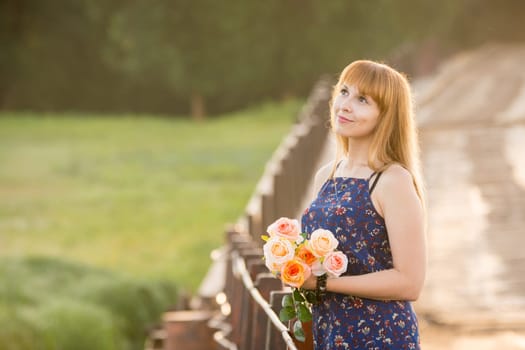 Young girl with a bouquet of roses standing on the bridge in the background blurred foliage