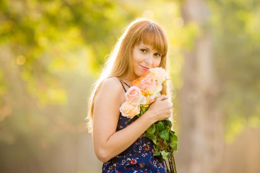 Beautiful young sexy girl standing with a bouquet of roses on a background of green sunny blurred