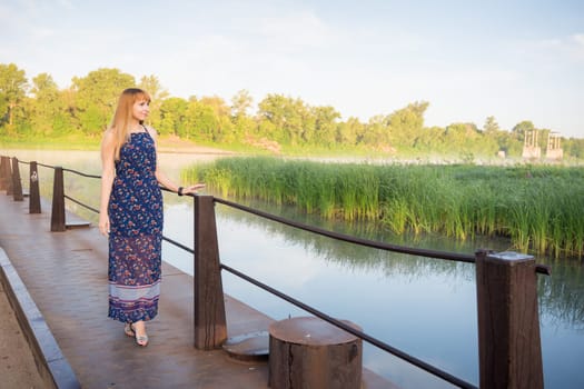 The charming young girl walking on the bridge over the river at dawn