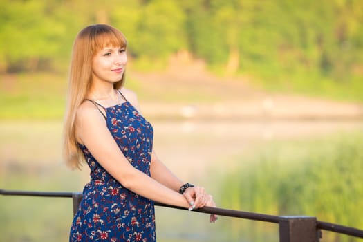 The charming young girl standing on a rustic bridge over the river at dawn sun