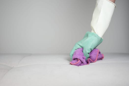 A person in gloves cleans a mattress with a pink and purple cloth.
