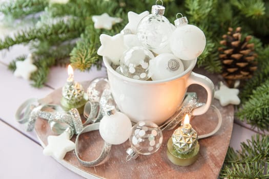 White cup with Christmas tree balls in front of fir branches