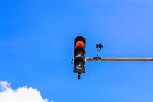 Traffic light and a security camera attached to a pole above the road.
