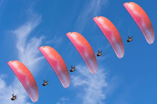 Five paragliders in a row in front of a blue sky..