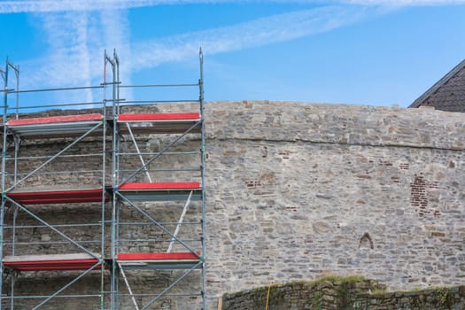Old city wall with scaffolding in front of blue sky..
