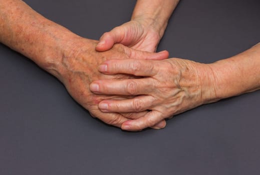 Hands of two loving senior people on a gray dark background