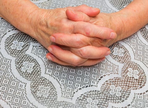 Hands of senior woman on a old tablecloth background