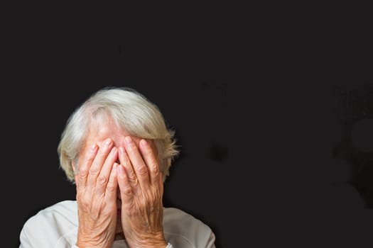 Portrait of an elderly woman with face closed by hands on black