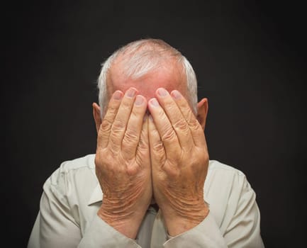Portrait of an elderly man with face closed by hands on black