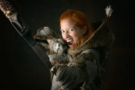 girl archer in a costume with bow isolated in a dark background