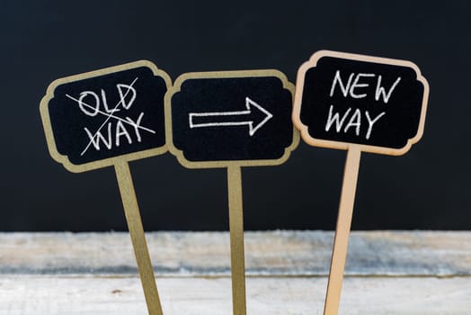 Concept message NEW WAY versus OLD WAY written with chalk on wooden mini blackboard labels, defocused chalkboard and wood table in background