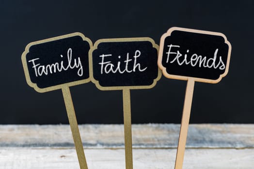 Concept message Family Faith Friends written with chalk on wooden mini blackboard labels, defocused chalkboard and wood table in background