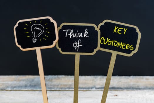 Concept message THINK OF KEY CUSTOMERS and light bulb as symbol for idea written with chalk on wooden mini blackboard labels, defocused chalkboard and wood table in background