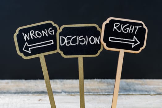 Concept message WRONG DECISION RIGHT DECISION written with chalk on wooden mini blackboard labels, defocused chalkboard and wood table in background