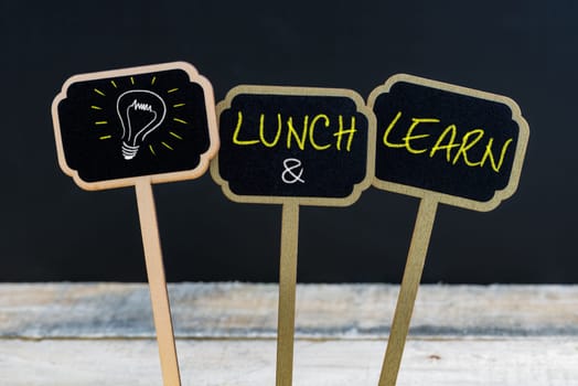 Concept message LUNCH and LEARN and light bulb as symbol for idea written with chalk on wooden mini blackboard labels, defocused chalkboard and wood table in background