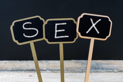 Text SEX written with chalk on wooden mini blackboard labels, defocused chalkboard and wood table in background
