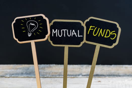 Concept message MUTUAL FUNDS and light bulb as symbol for idea written with chalk on wooden mini blackboard labels, defocused chalkboard and wood table in background
