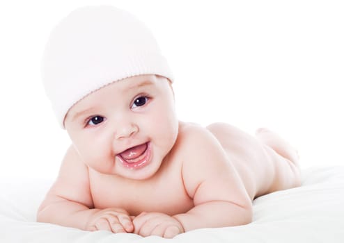 Happy baby lying on stomach on white floor background, wearing a cap and smiling big.