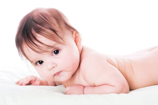 Happy baby lying on stomach on white floor background, wearing a cap and smiling big.