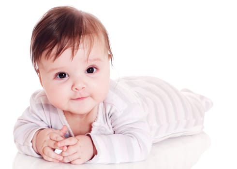 Happy baby lying on stomach on white floor background, wearing a cap and smiling big.