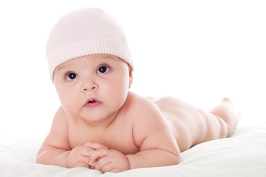 Happy baby lying on stomach on white floor background, wearing a cap and smiling big.