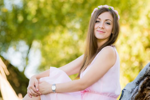 Beautiful girl sits on a background illuminated by the sun leaves