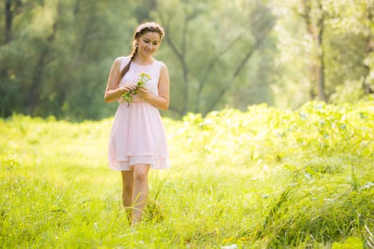 Young girl in the summer light dress collecting wild flowers