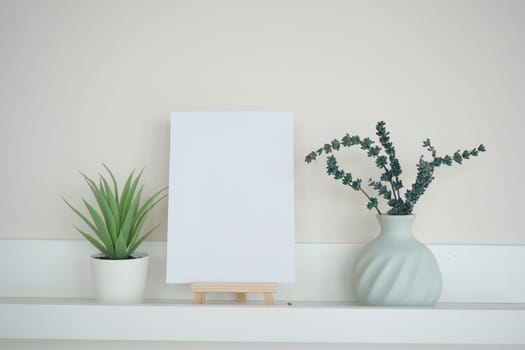A shelf displays a blank canvas between two decorative plants.
