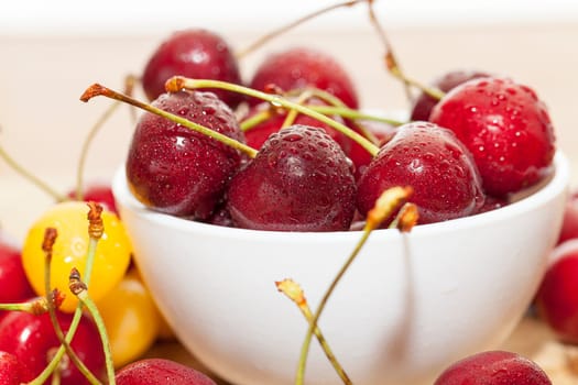 Photographed close-up ripe red cherries covered with drops of water, little depth of field, berries are on a wooden table in a white bowl