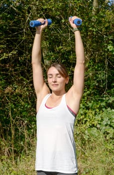 Fitness woman doing exercises with blue dumbbells in the countryside