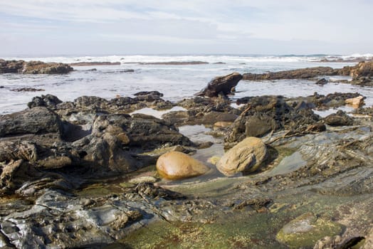 Two big boulders lie in the water of a rock pool on a rugged coastline.