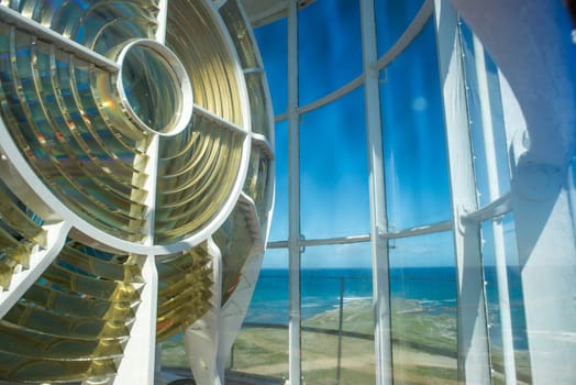 An up close view of the light of the Cape Agulhas lightouse with a view of the ocean in the background.