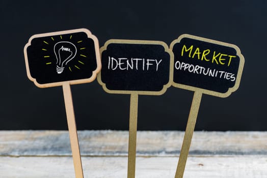 Concept message IDENTIFY MARKET OPPORTUNITIES and light bulb as symbol for idea written with chalk on wooden mini blackboard labels, defocused chalkboard and wood table in background