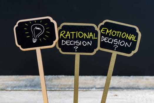 Concept message RATIONAL DECISION versus EMOTIONAL DECISION and light bulb as symbol for idea written with chalk on wooden mini blackboard labels, defocused chalkboard and wood table in background