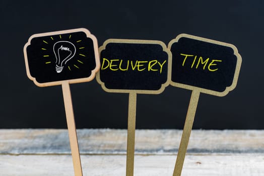 Concept message DELIVERY TIME and light bulb as symbol for idea written with chalk on wooden mini blackboard labels, defocused chalkboard and wood table in background