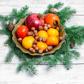 dish with tangerines,pomegranates,persimmons and nuts,decorated with fir branches