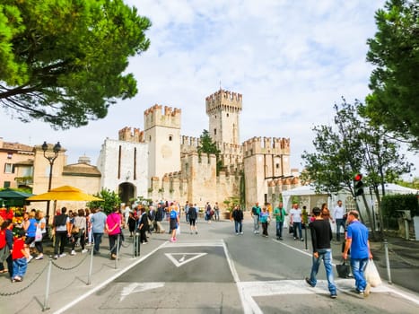 Sirmione, Italy - September 20, 2014: The people going to the Scaliger Castle. The famous castle of Sirmione and its small port are an uncommon example of a fortress used as a port. The building of this complex started in 1277 by Mastino della Scala.