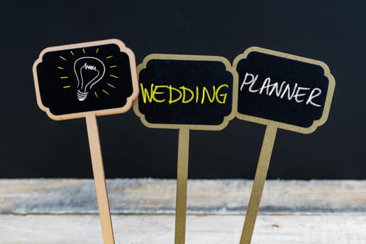 Concept message WEDDING PLANNER and light bulb as symbol for idea written with chalk on wooden mini blackboard labels, defocused chalkboard and wood table in background