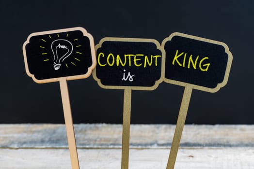 Concept message CONTENT IS KING and light bulb as symbol for idea written with chalk on wooden mini blackboard labels, defocused chalkboard and wood table in background